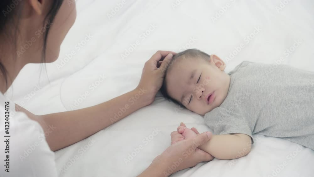 Young asian mother touch hand of little baby girl with tender on bed in the bedroom, mom love newborn and care, woman with expression with child together, parent and daughter, family concept. Young asian mother touch hand of little baby girl with tender on bed in the bedroom, mom love newborn and care, woman with expression with child together, parent and daughter, family concept.