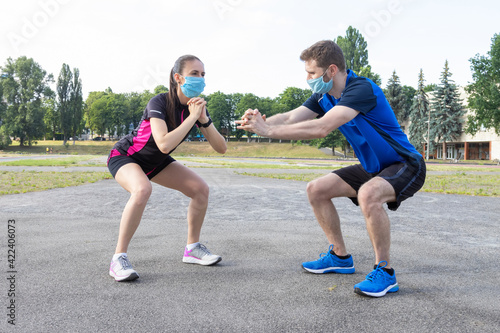 Couple together go fitness workout outdoors during quarantine. Sports activities in pairs, wearing protective masks on their faces.