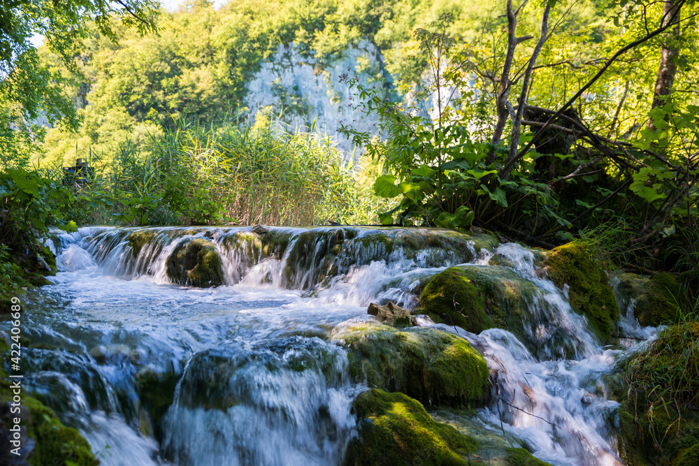 Small waterfall in river with stones covered by moss and trees and redds in background. Small waterfall in river with stones covered by moss and trees and redds in background.