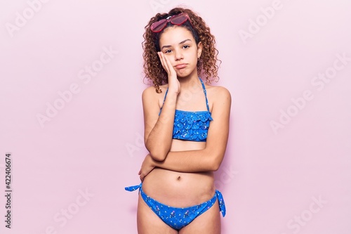 Beautiful kid girl with curly hair wearing bikini and sunglasses thinking looking tired and bored with depression problems with crossed arms.