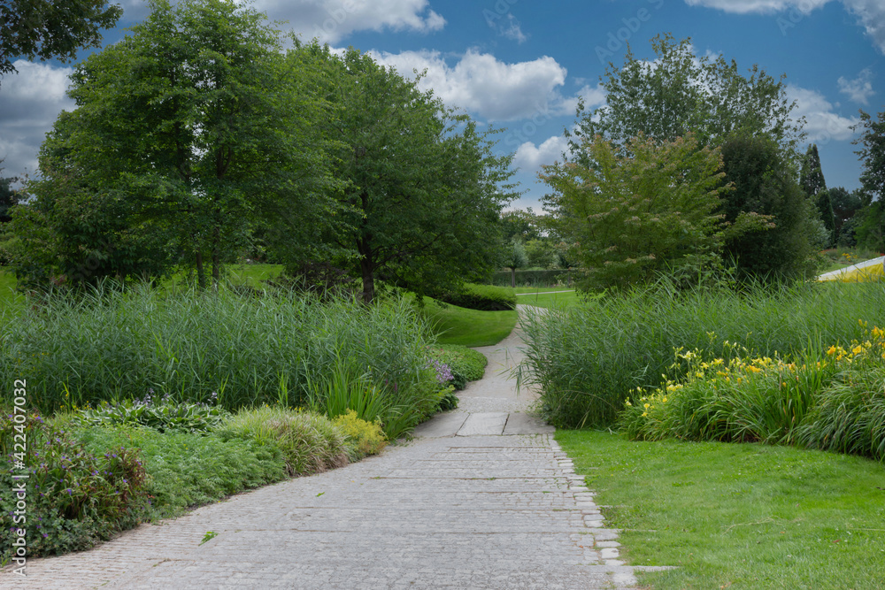 Walk in the park, beautiful landscaped garden with lush grass and colorful flowerbed under cloudy blue sky Walk in the park, beautiful landscaped garden with lush grass and colorful flowerbed under cloudy blue sky