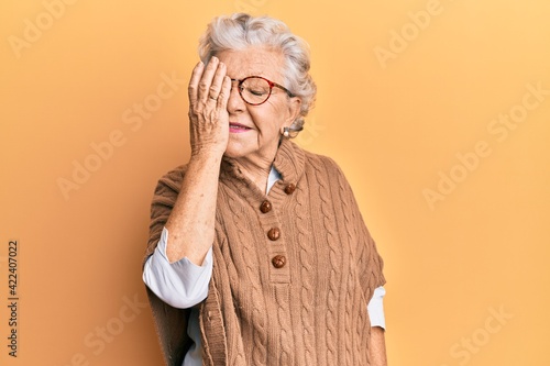 Senior grey-haired woman wearing casual clothes and glasses covering one eye with hand, confident smile on face and surprise emotion. © Krakenimages.com