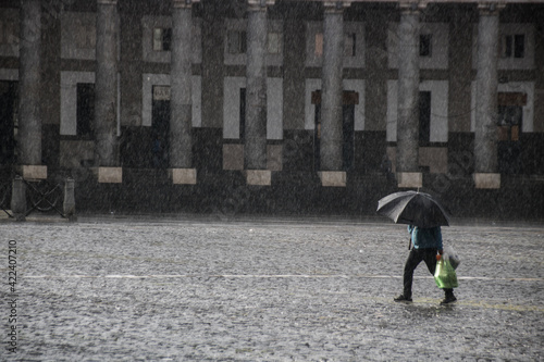 personne sous une forte averse de pluie avec un parapluie sur une place pavée photo