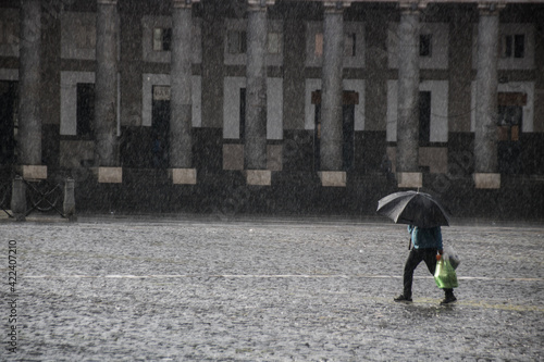 Tableau sur toile personne sous une forte averse de pluie avec un parapluie sur une place pavée