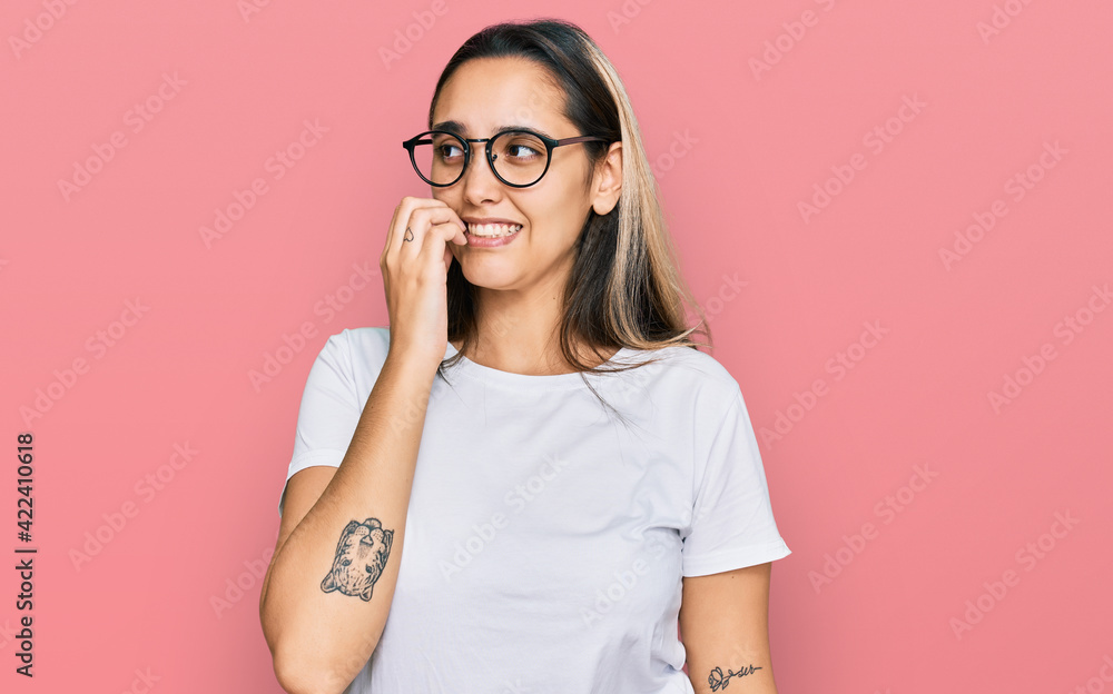 Young hispanic woman wearing casual white t shirt looking stressed and nervous with hands on mouth biting nails. anxiety problem.