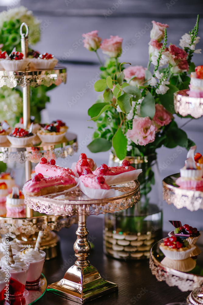 Wedding decoration of a candy bar in pink and green colors. Eclairs and panna cotta. Fresh flowers for the holiday. Sweets and tasty. Celebration and floristic concept