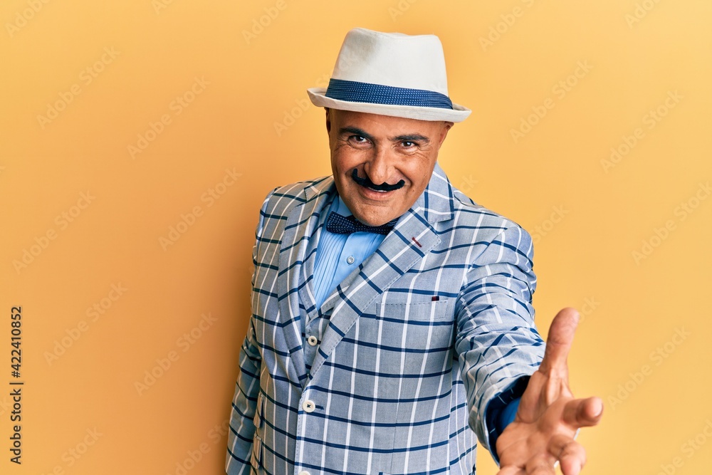 Mature middle east man with mustache wearing vintage and elegant fashion style smiling friendly offering handshake as greeting and welcoming. successful business.