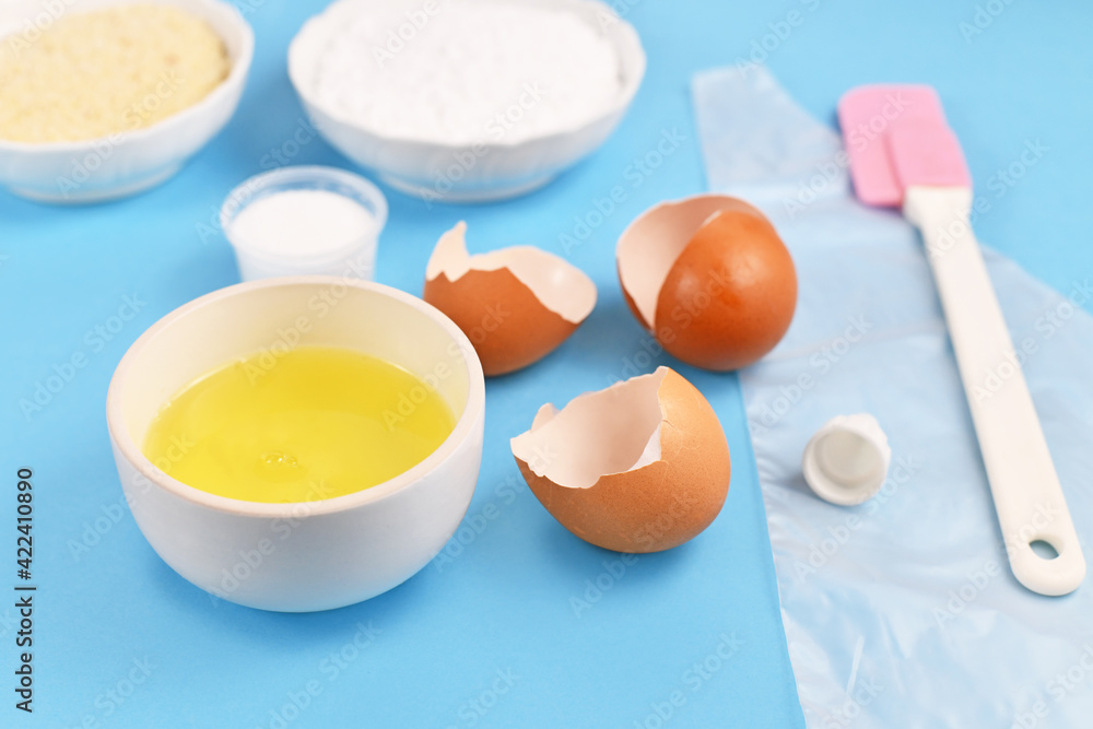 Ingredients for making homemade French Macarons with bowl with egg white next to broken eggshells on blue background Ingredients for making homemade French Macarons with bowl with egg white next to broken eggshells on blue background