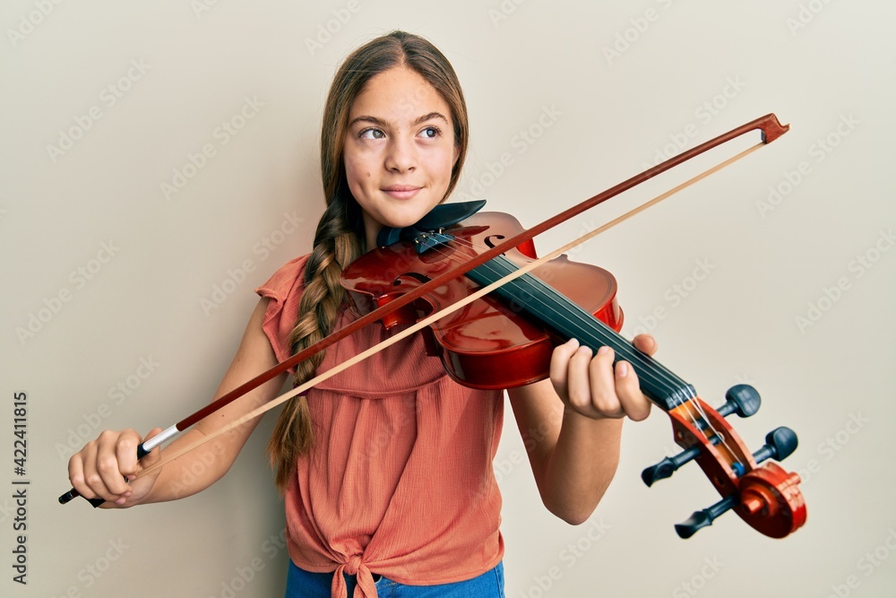 Beautiful brunette little girl playing violin smiling looking to the side and staring away thinking. Beautiful brunette little girl playing violin smiling looking to the side and staring away thinking.