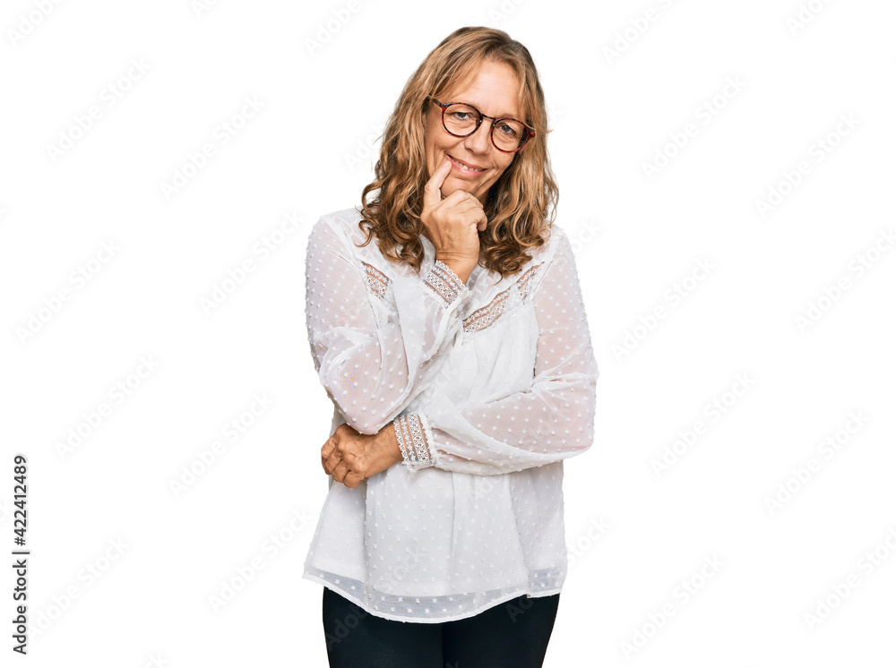 Middle age blonde woman wearing casual white shirt and glasses looking confident at the camera with smile with crossed arms and hand raised on chin. thinking positive. Middle age blonde woman wearing casual white shirt and glasses looking confident at the camera with smile with crossed arms and hand raised on chin. thinking positive.
