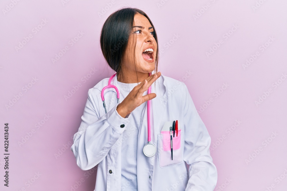 Beautiful hispanic woman wearing doctor uniform and stethoscope shouting and screaming loud to side with hand on mouth. communication concept. Beautiful hispanic woman wearing doctor uniform and stethoscope shouting and screaming loud to side with hand on mouth. communication concept.