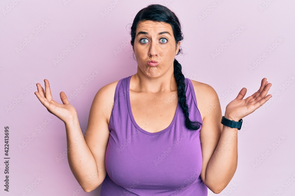 Plus size brunette woman wearing sportswear clueless and confused with open arms, no idea and doubtful face. Plus size brunette woman wearing sportswear clueless and confused with open arms, no idea and doubtful face.