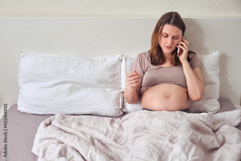 An excited pregnant woman is talking on the phone while lying in bed An excited pregnant woman is talking on the phone while lying in bed