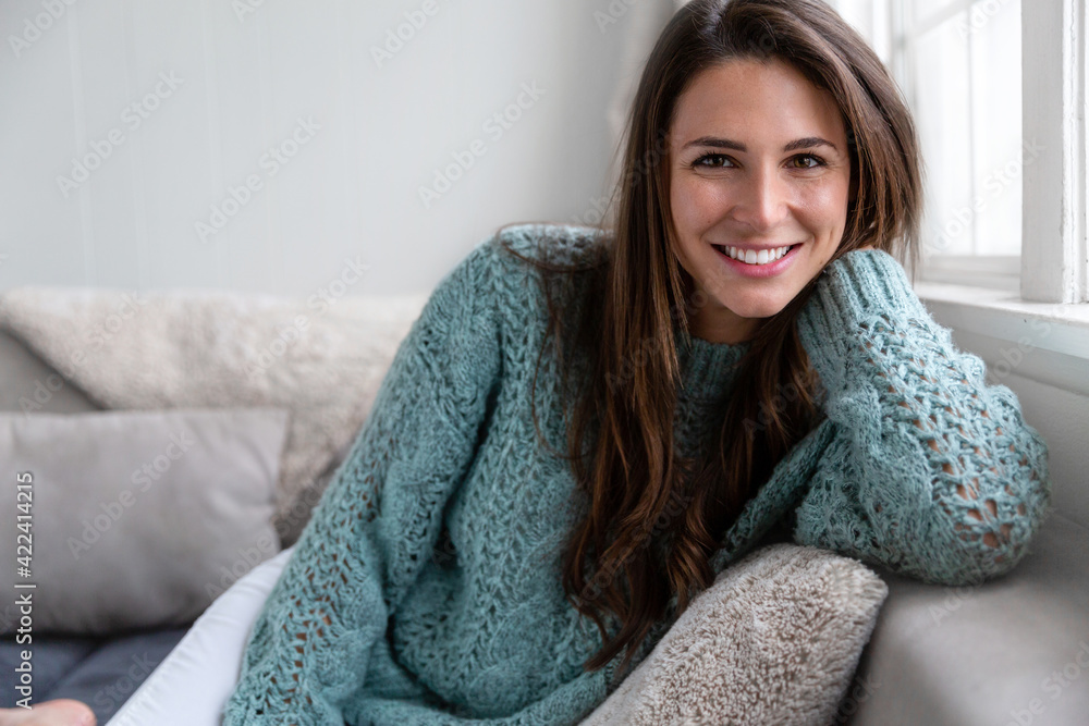 Beautiful lifestyle portrait of a happy female brunette with perfect white teeth, smiling cheerfully in a bright living room next to a window Beautiful lifestyle portrait of a happy female brunette with perfect white teeth, smiling cheerfully in a bright living room next to a window
