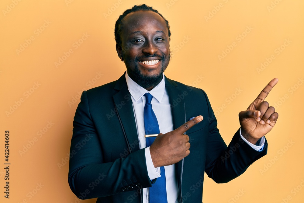 Handsome young black man wearing business suit and tie smiling and looking at the camera pointing with two hands and fingers to the side. Handsome young black man wearing business suit and tie smiling and looking at the camera pointing with two hands and fingers to the side.