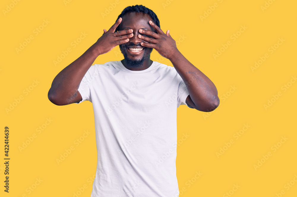 Young african american man with braids wearing casual white tshirt covering eyes with hands smiling cheerful and funny. blind concept. Young african american man with braids wearing casual white tshirt covering eyes with hands smiling cheerful and funny. blind concept.