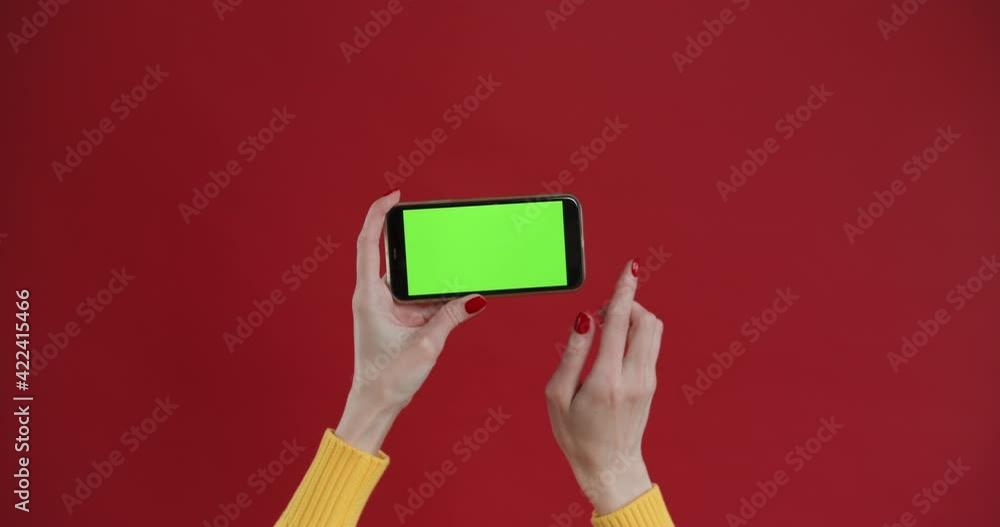 Hand using phone with green screen, chroma key. Touch and swiping on red background. Top horizon view. Mock up. Hand using phone with green screen, chroma key. Touch and swiping on red background. Top horizon view. Mock up.