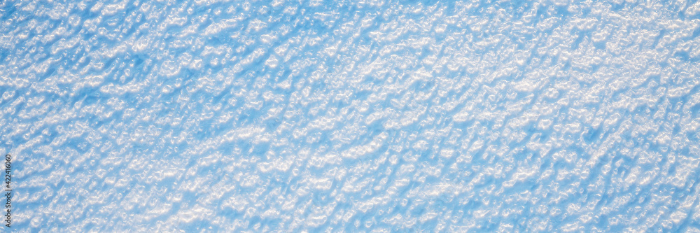Obraz premium Beautiful winter background with snowy ground. Natural snow texture. Wind sculpted patterns on snow surface. Wide panoramic texture for background and design.