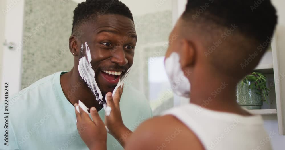 African american boy putting shaving cream on his father face and laughing together African american boy putting shaving cream on his father face and laughing together