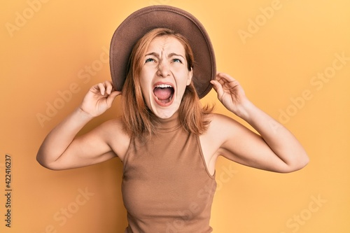 Young caucasian woman wearing hat angry and mad screaming frustrated and furious, shouting with anger looking up.