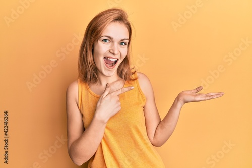 Young caucasian woman wearing casual style with sleeveless shirt amazed and smiling to the camera while presenting with hand and pointing with finger.