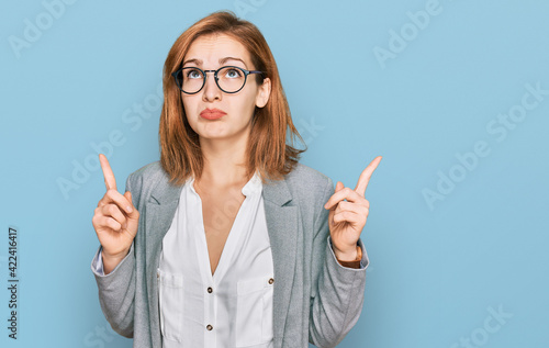 Foto Young caucasian woman wearing business style and glasses pointing up looking sad and upset, indicating direction with fingers, unhappy and depressed
