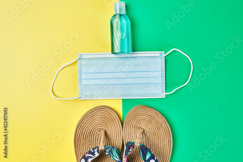 Studio photo, summer sandals on two colors yellow and green vertical background, antiseptic gel and face mask ready for holidays