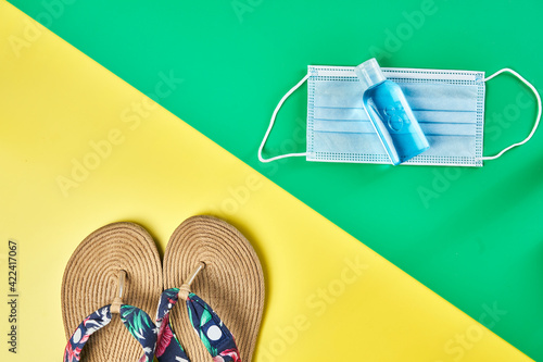 Studio photo, diagonal summer sandals on two colors yellow and green vertical background, antiseptic gel and face mask ready for holidays