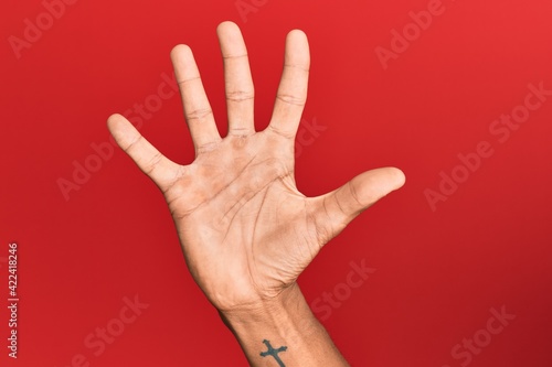 Hand of hispanic man over red isolated background counting number 5 showing five fingers