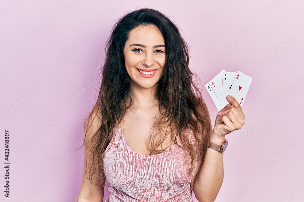 Young hispanic woman holding poker cards looking positive and happy standing and smiling with a confident smile showing teeth Young hispanic woman holding poker cards looking positive and happy standing and smiling with a confident smile showing teeth