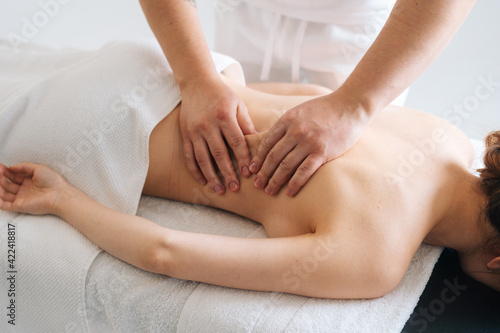 Male masseur massaging back of young unrecognizable woman lying on massage table. Beautiful female with perfect skin getting relaxing massage. Concept of massage spa treatments.