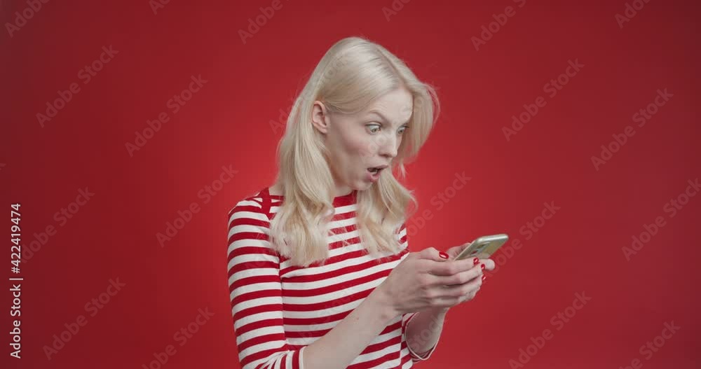 Young woman playing games using smartphone, winer shows green screen of smartphone standing isolated over a red background Young woman playing games using smartphone, winer shows green screen of smartphone standing isolated over a red background