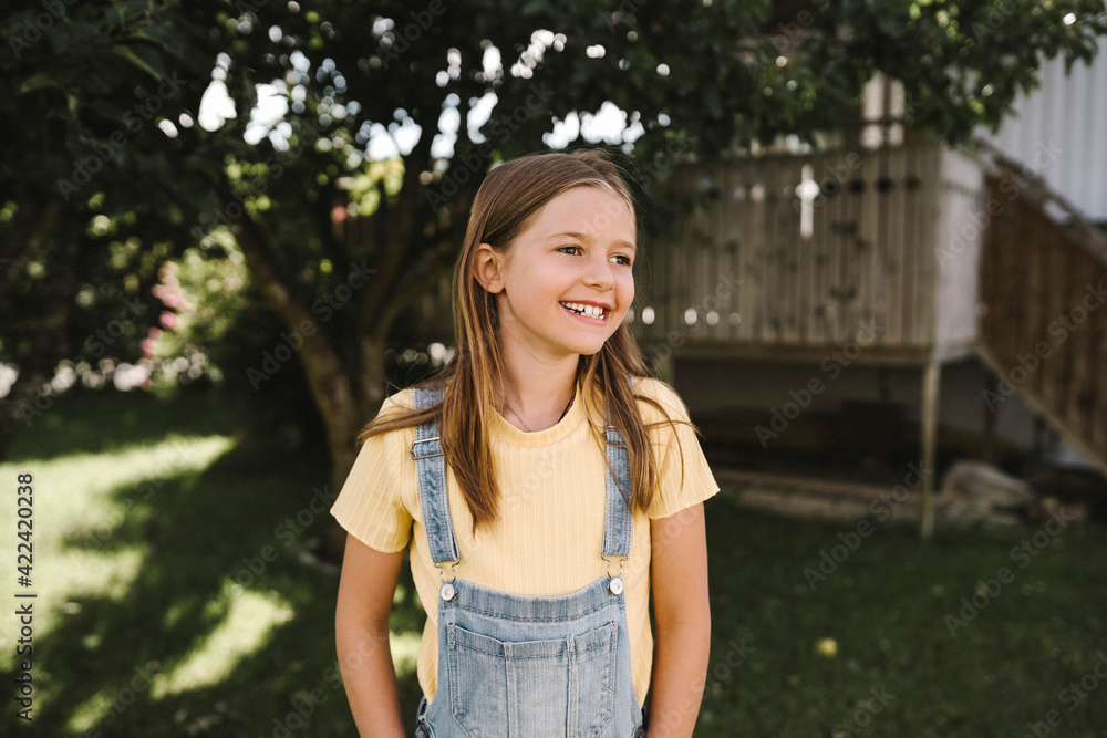 Smiling girl looking away while standing in back yard Smiling girl looking away while standing in back yard