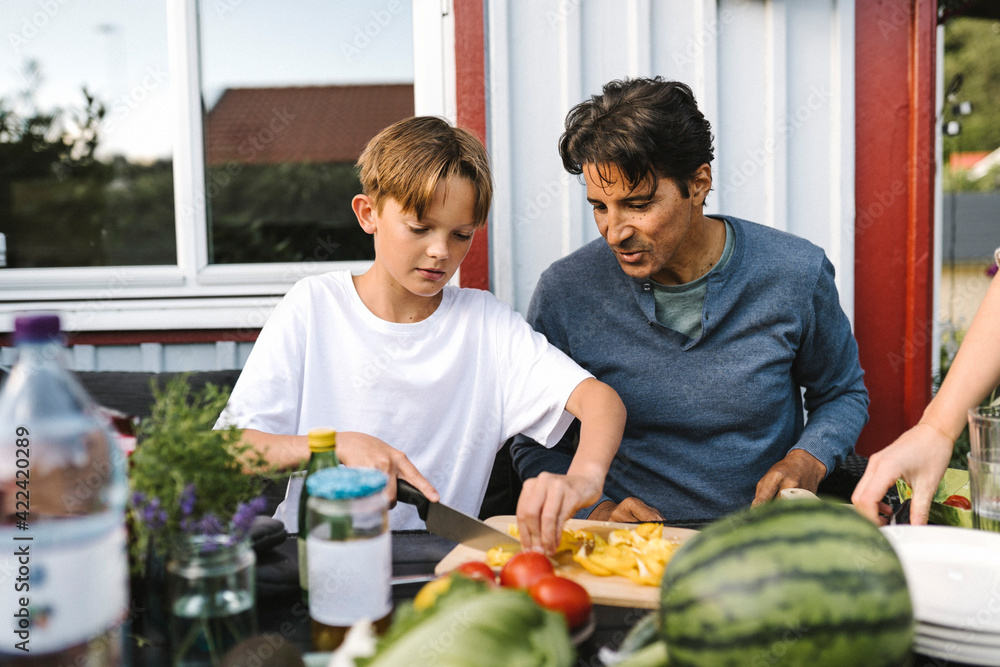 Son cutting vegetable sitting by father in balcony Son cutting vegetable sitting by father in balcony