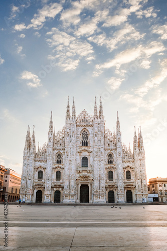 View of the Milan Cathedral with empty square due to the coronavirus blockade, with blue sky with white clouds and glow of light from the newly risen sun, vertical