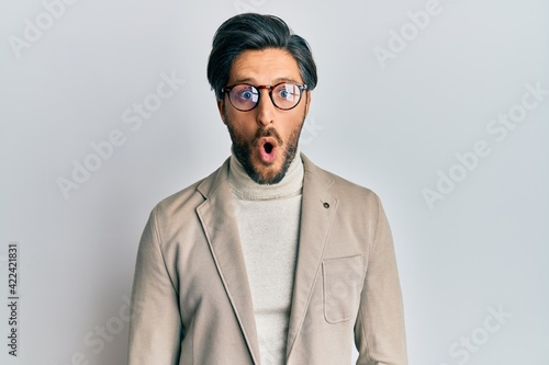 Young hispanic man wearing business jacket and glasses afraid and shocked with surprise expression, fear and excited face.