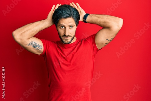Young hispanic man wearing casual red t shirt doing bunny ears gesture with hands palms looking cynical and skeptical. easter rabbit concept.