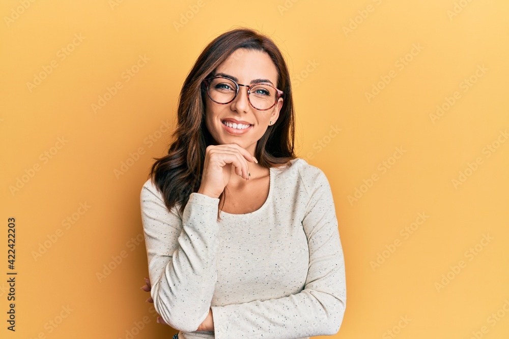 Young brunette woman wearing casual clothes and glasses smiling looking confident at the camera with crossed arms and hand on chin. thinking positive.