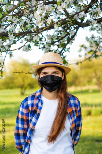 Portrait of young woman wearing black face mask. Dust protection against virus. Coronavirus pandemic time. Girl in American country style. Lifestyle concept. Selective focus. © tanitost