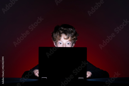 Surprised boy with computer surfing the internet alone on dark background