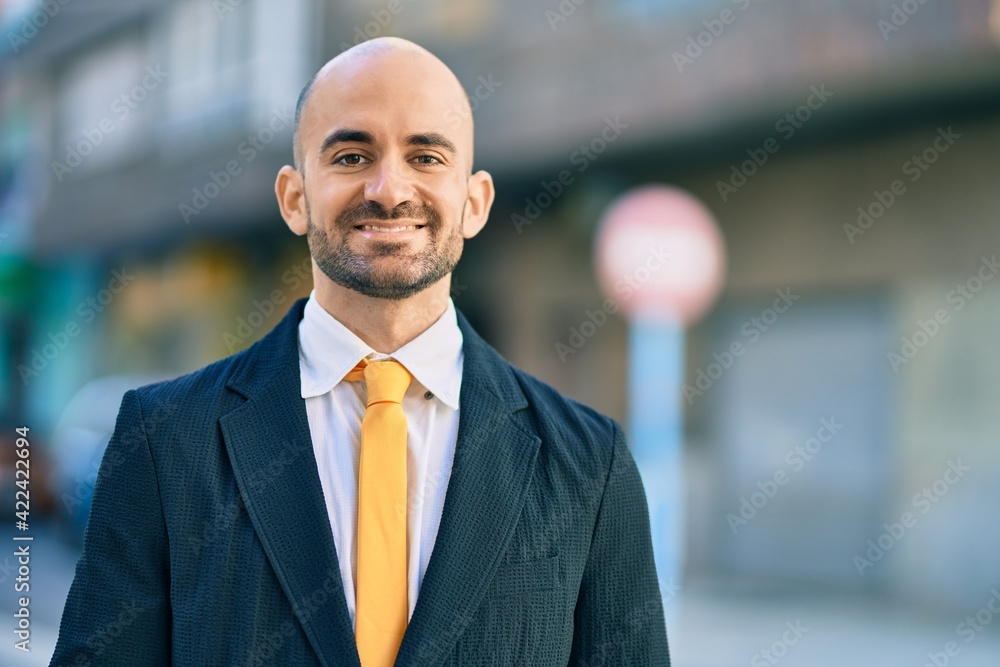 Fototapeta premium Young hispanic bald businessman smiling happy standing at the city.