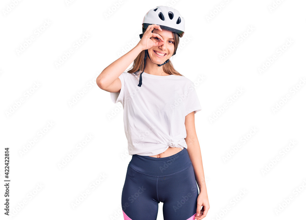 Young beautiful girl wearing bike helmet smiling happy doing ok sign with hand on eye looking through fingers Young beautiful girl wearing bike helmet smiling happy doing ok sign with hand on eye looking through fingers