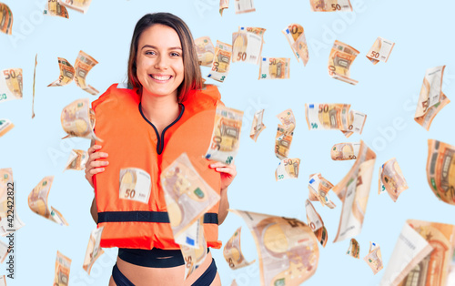 Young beautiful girl wearing life jacket looking positive and happy standing and smiling with a confident smile showing teeth