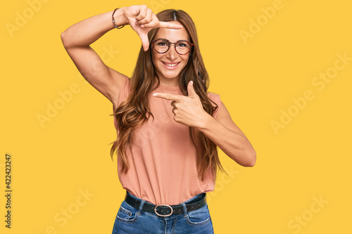 Young hispanic woman wearing casual clothes and glasses smiling making frame with hands and fingers with happy face. creativity and photography concept.