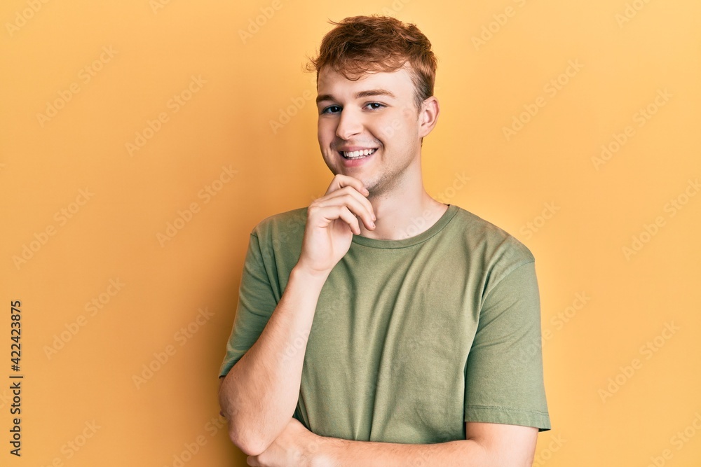 Young caucasian man wearing casual green t shirt smiling looking confident at the camera with crossed arms and hand on chin. thinking positive. Young caucasian man wearing casual green t shirt smiling looking confident at the camera with crossed arms and hand on chin. thinking positive.