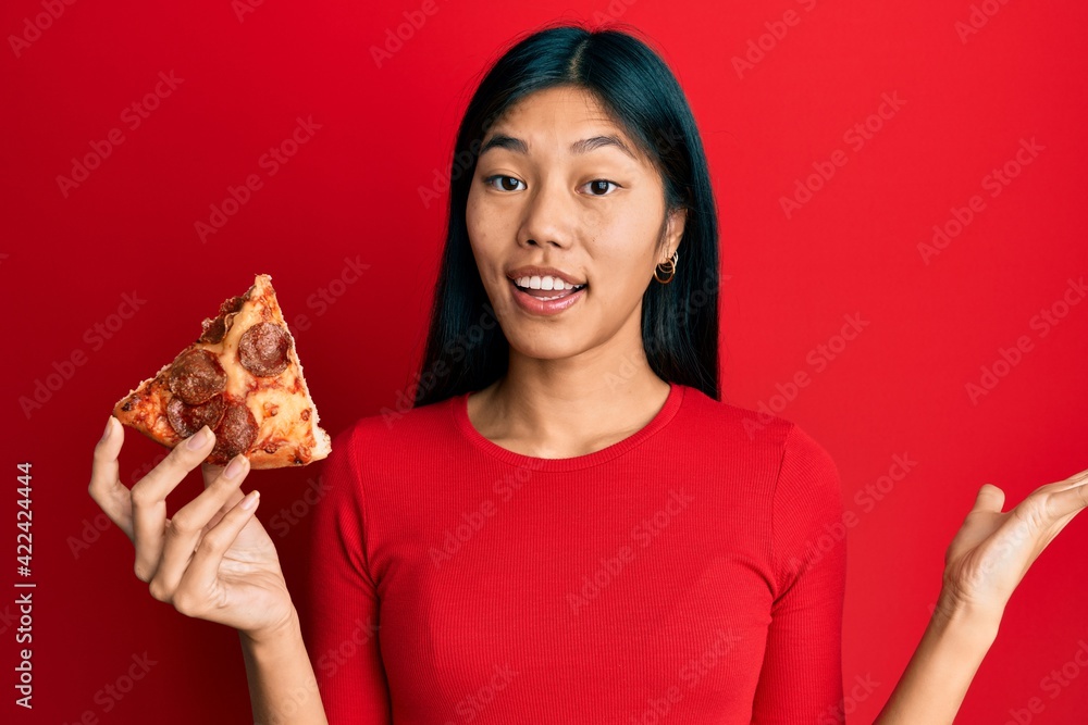 Young chinese woman holding italian pizza celebrating victory with happy smile and winner expression with raised hands Young chinese woman holding italian pizza celebrating victory with happy smile and winner expression with raised hands