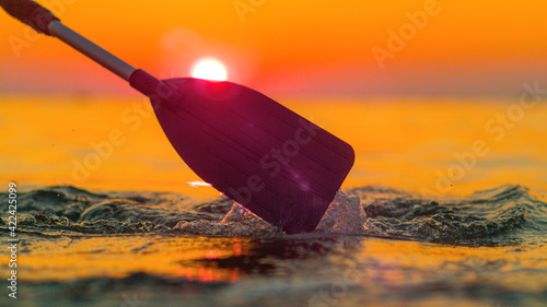 Konstfotografi SILHOUETTE: Golden sunset shines on the kayaker's paddle splashing ocean water