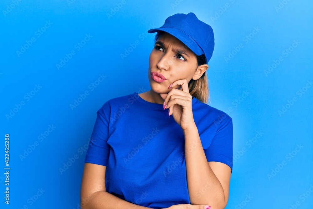 Beautiful brunette woman wearing delivery uniform serious face thinking about question with hand on chin, thoughtful about confusing idea Beautiful brunette woman wearing delivery uniform serious face thinking about question with hand on chin, thoughtful about confusing idea