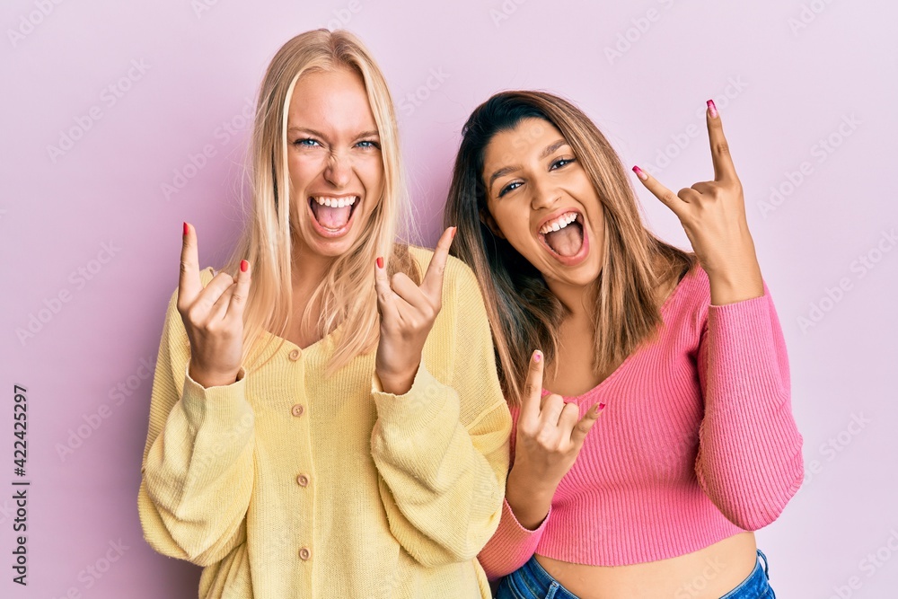Two friends standing together over pink background shouting with crazy expression doing rock symbol with hands up. music star. heavy concept. Two friends standing together over pink background shouting with crazy expression doing rock symbol with hands up. music star. heavy concept.
