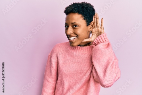 Young african american girl wearing casual clothes smiling with hand over ear listening and hearing to rumor or gossip. deafness concept.